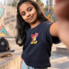 Blue crop T-shirt for girls with colourful front and back graphic prints, paired with light blue jeans.